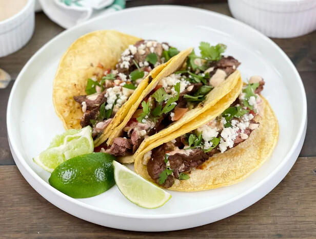 Taqueria Style Carne Asada Tacos - Marinated steak on a corn tortilla, topped with onions, fresh cilantro, cotija cheese, and severed with a side of our house made salsa verde and lime wedge.